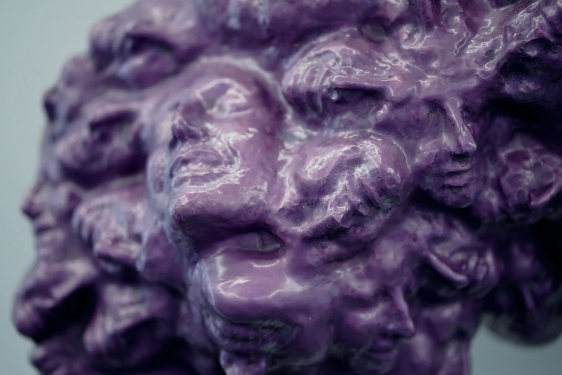 Detaliu al unei sculpturi violet cu multe chipuri în relief